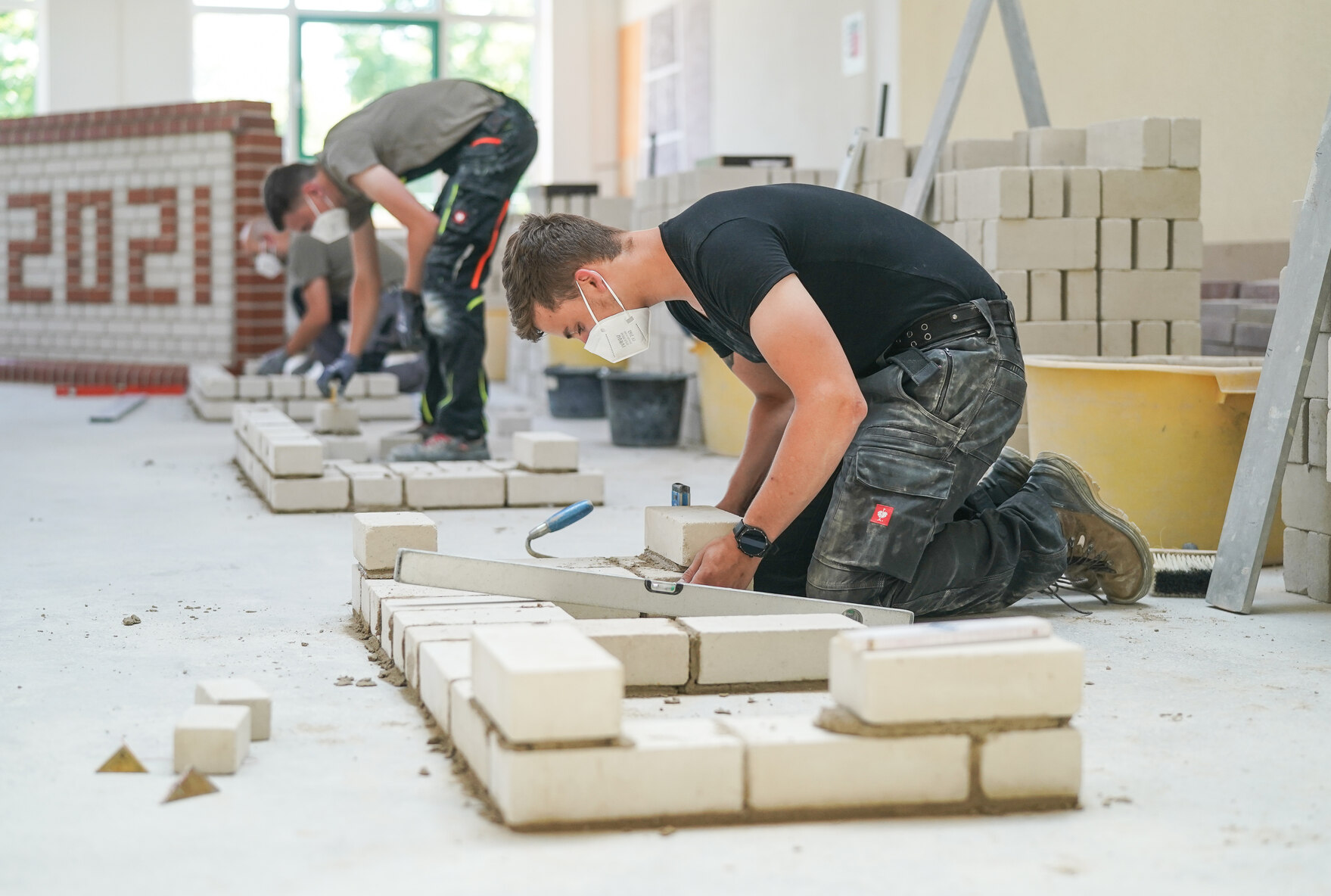 Auszubildende mauern in der Werkstatt des Überbetrieblichen Ausbildungszentrums Bau Bildung e. V. in Leipzig an einer Übungsmauer.