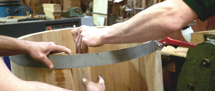 Die Arme zweier Männer beim Bau eines Holzfasses in einer Böttcherei.